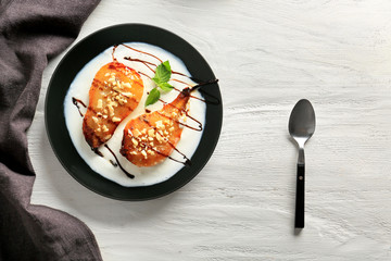 Plate with tasty baked pears and melted ice cream on light wooden table
