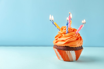 Delicious birthday cupcake with candles on color background