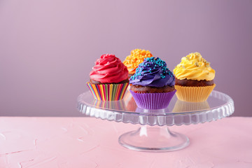 Glass dessert stand with delicious cupcakes on color background