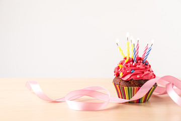 Delicious birthday cupcake with burning candles and ribbon on light wooden table