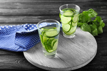 Glasses of fresh cucumber water on wooden board