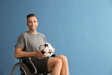 Young man with ball sitting in wheelchair against color background