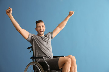 Happy young man sitting in wheelchair against color background