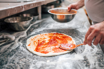 Close-up image of chef preparing the pizza base with tomato sauce. - obrazy, fototapety, plakaty