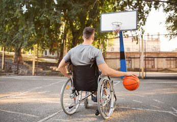 Young man in wheelchair playing basketball outdoors
