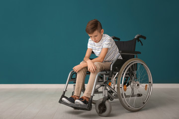 Depressed boy in wheelchair against color wall
