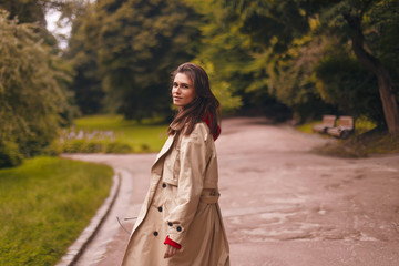 Portrait of woman wearing beige trench coat, red hoodie while walking in park. she look happy.