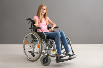 Fototapeta na wymiar Teenage girl in wheelchair against grey wall