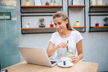 Casual young woman with laptop in the cafe, drinking lemonade and coffee.