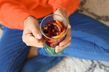 Woman holding glass cup of delicious mulled wine while sitting on floor