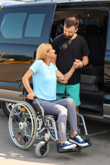 Man helping woman in wheelchair to sit in car