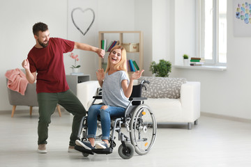 Beautiful woman in wheelchair with man dancing at home