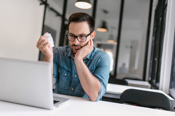 Annoyed casual man working in office while crumpling paper and looking at laptop.