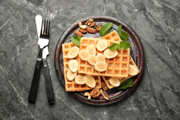 Delicious waffles with banana slices and nuts on dark table
