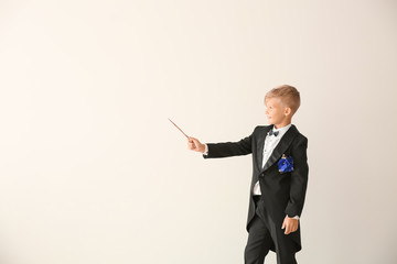 Cute little magician showing tricks on light background