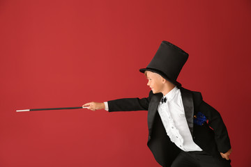 Cute little magician showing tricks on color background