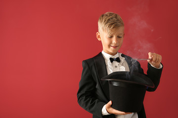 Cute little magician showing trick with hat on color background