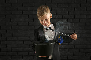Cute little magician showing trick with hat against dark brick wall