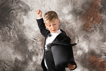 Cute little magician showing trick with hat on grunge background