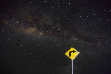 yellow right turn road sign with milky way background at night