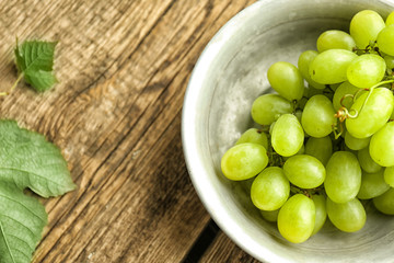Bowl with sweet grapes on wooden table