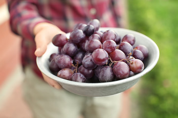 Woman holding bowl with sweet grapes outdoors, closeup