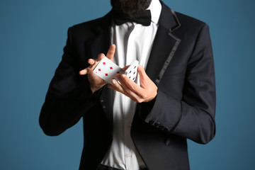 Magician showing tricks with cards on color background, closeup