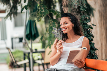 Enjoying on the vacation. Young woman smelling lavander and reading a book outdoors.
