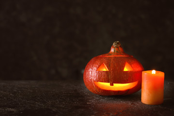 Halloween pumpkin with burning candle on dark background