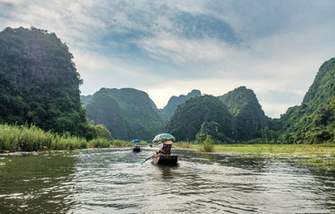Fototapeta na wymiar Ancient boating with vietnamese using foot paddle and view limestone mountain