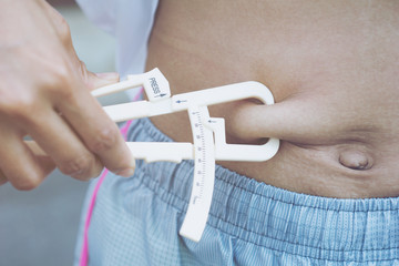 Close-up Of Hands measuring his body fat of sporty woman with calipers.Weight loss concept