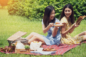 Couple of girls going picnic in a park, reading a book together and feeling friendly.
