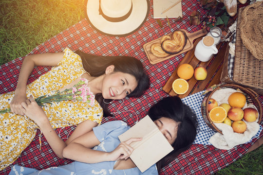 Couple of girls going picnic in a park, reading a book together and feeling friendly.