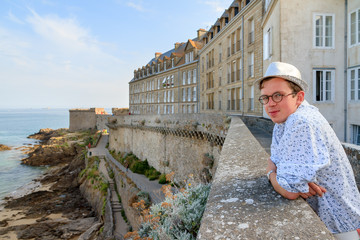 Tourist enjoys the ocean view from the wall of the historic city Saint-Malo in Brittany, France, a major summer vacation tourist destination - obrazy, fototapety, plakaty