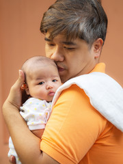 Portrait of happy Asia father holding his newborn sweet baby dressed in white clothes. The father embracing his baby with love and care. his daughter always happy when he is held.