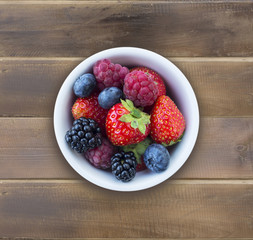 Top view. Fruits and berries in bowl on wooden background. Ripe raspberries, strawberries, blackberries and blueberries. Background of mix fruits with copy space for text. 