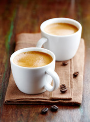 Two cups of espresso on rustic wooden table. Symbolic image. Coffee and coffee beans. Rustic wooden background. Close up.