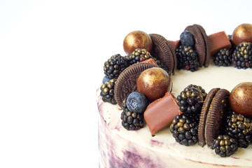 Cake with white and black cream, decorated with blueberries, blackberry, chocolate chip cookies, candies, bars and gold on a white background. Picture for a menu or a confectionery catalog.