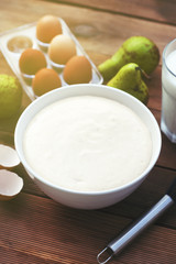 Ingredients for baking pie with pears. The process of making sweet pastries. Bowl with dough, glass of milk, eggs and pear fruits. Wooden table.