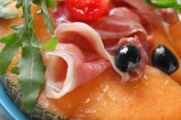 Delicious melon with prosciutto, olives and arugula on plate, closeup