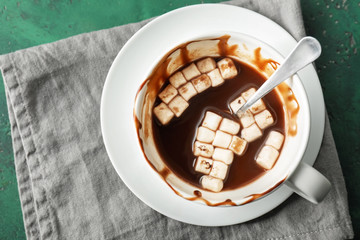 Half empty cup of hot chocolate with marshmallows on color table