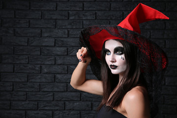 Beautiful woman dressed as witch for Halloween with magic wand on dark background