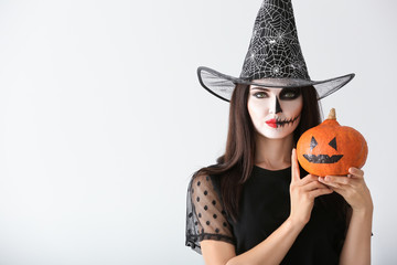 Beautiful woman dressed as witch for Halloween with pumpkin on light background