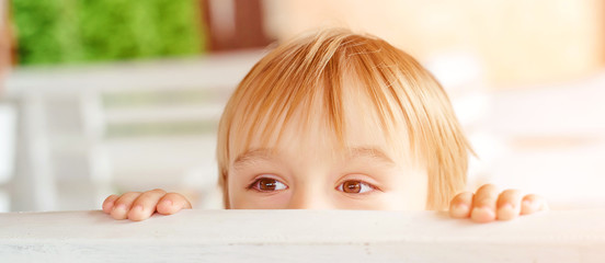 Cute little boy hiding behind a bench outdoors. Child having fun outside. Game of hide and seek....