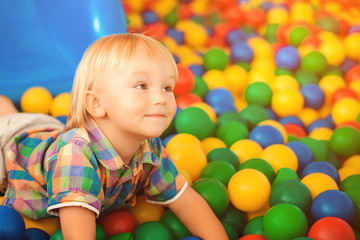 Fototapeta na wymiar Happy baby at playground. Little child at indoor play center. Happy childhood. Child playing with colorful balls in playground ball pool. Child boy playing and smiling.