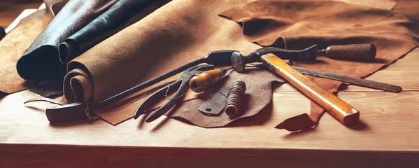 Fotobehang Shoemaker's work desk. Tools and leather at cobbler workplace. Set of leather craft tools on wooden background. Shoes maker tools on wooden table. © volurol