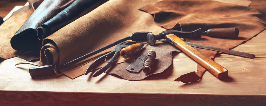 Shoemaker's work desk. Tools and leather at cobbler workplace. Set of leather craft tools on wooden background. Shoes maker tools on wooden table.