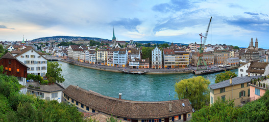 Beautiful panorama of the city of Zurich, Switzerland, at the river Limmat after sunset in the blue hour with the crane and Grossmünster  church on the skyline