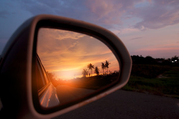 Evening sunlight of countryside viewed from the car's side mirrors.