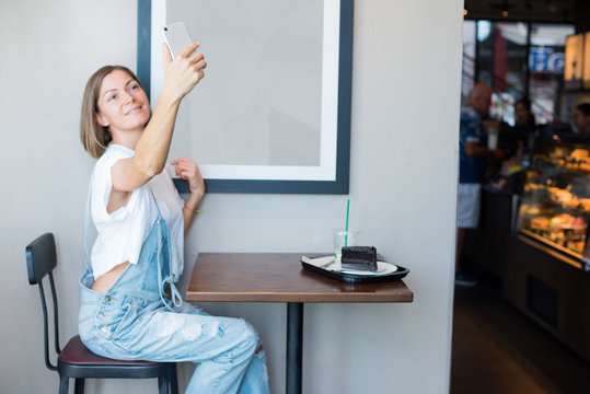 young woman wearing overalls tshirt taking selfie